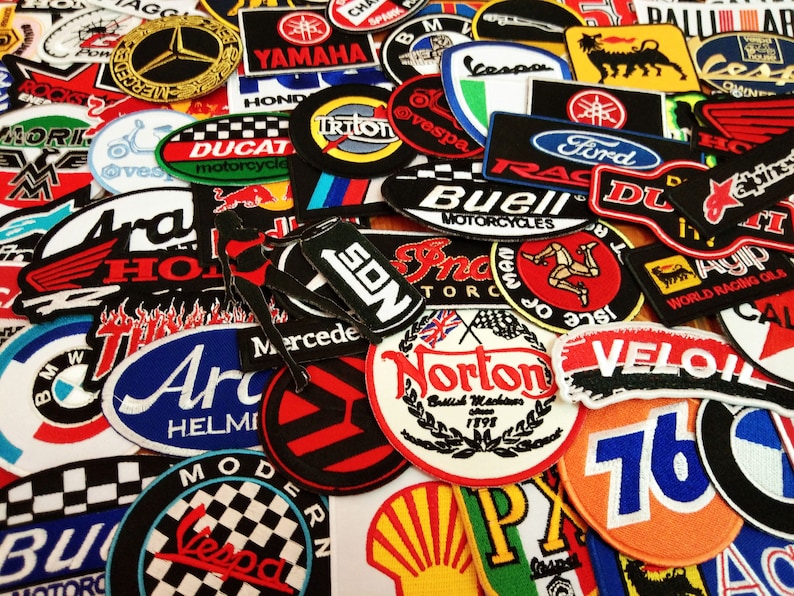 May include: A collection of colorful embroidered patches featuring various logos and designs, including motorcycle brands, racing teams, and vehicle manufacturers. The patches are made of fabric and have a variety of shapes and sizes.