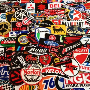 May include: A collection of colorful embroidered patches featuring various motorcycle and automotive brands, including Yamaha, Honda, Ducati, Ford, and Michelin. The patches are arranged in a random pattern and are all different sizes and shapes.