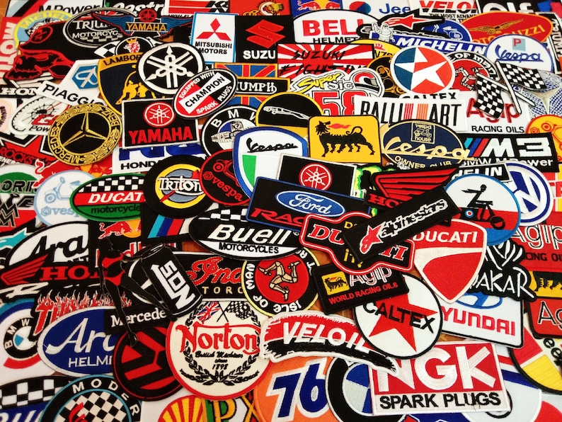 May include: A collection of colorful embroidered patches featuring various motorcycle and automotive brands, including Yamaha, Honda, Ducati, Ford, and Michelin. The patches are arranged in a random pattern and are all different sizes and shapes.