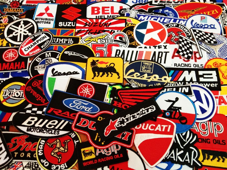 May include: A collection of colorful embroidered patches featuring various motorcycle, car, and racing brands. The patches include logos for Yamaha, Suzuki, Vespa, Ford, Ducati, Agip, and more.