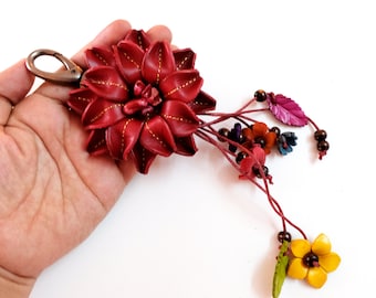Könnte beinhalten: Ein roter Lederblumen-Schlüsselanhänger mit einem Metallverschluss und einem Anhänger aus kleineren Lederblumen und Perlen.