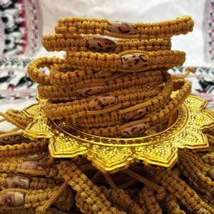 May include: A stack of gold braided bracelets with brown and white patterned beads. The bracelets are displayed on a gold decorative stand.