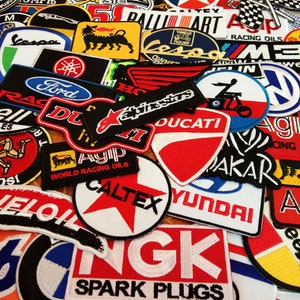 May include: A collection of colorful embroidered patches featuring various logos and brand names, including Vespa, Ford, Ducati, Agip, Caltex, and Hyundai. The patches are arranged in a random pattern and are perfect for adding a touch of personality to jackets, bags, or other items.