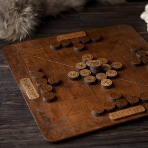 May include: A wooden board game with a grid pattern and carved details. The game pieces are small, round wooden tokens with etched designs. The board and pieces are a warm brown color, suggesting a rustic or vintage aesthetic.