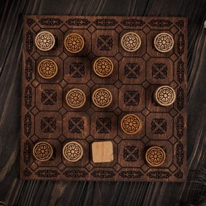 Könnte beinhalten: Holzbrettspiel in Dunkelbraun mit einem Rastermuster und dekorativen floralen Designs. Das Spiel enthält hellbraune, kreisförmige Spielsteine mit aufwendigen Mustern. Das Brett misst ca. 30 cm x 30 cm.