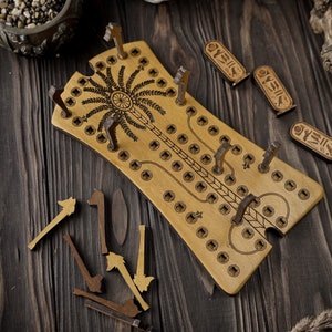 Può includere: Un tabellone da gioco in legno con un design a forma di palma e buchi per i pioli. Il tabellone è marrone e ha una finitura marrone chiaro. Ci sono diversi pioli in legno e piccoli pezzi di legno con geroglifici su di essi.