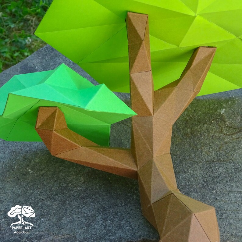 May include: A detailed paper art tree with a brown trunk and bright green leaves. The tree's geometric design is visible, with the leaves and branches constructed from folded paper. The tree is set against a gray background.
