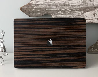 Puede incluir: Un ordenador portátil con un diseño de vetas de madera marrón oscuro y negro. El logotipo de Apple es visible en el centro. El portátil está sobre una superficie blanca, con una estatua de ciervo plateado a la izquierda y una decoración de madera envejecida en el fondo.