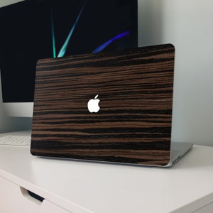 MacBook with a sleek dark wood grain cover featuring rich brown and black stripes, precisely fitted to the laptop’s lid with the Apple logo cutout in the center, creating a modern, natural, and stylish look.