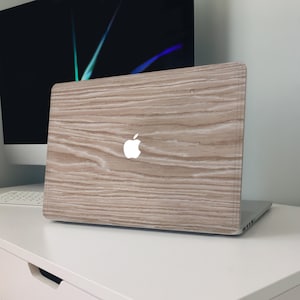 May include: A laptop with a light brown wood grain design. The Apple logo is visible on the lid. The laptop is on a white surface, with a computer monitor in the background.