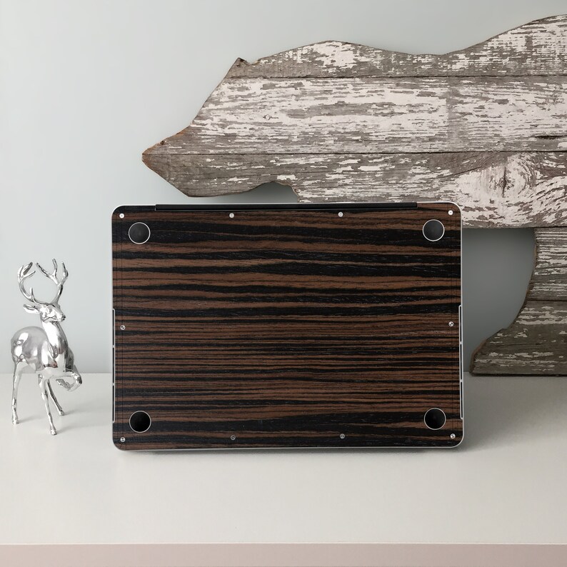 May include: A black and brown wood-grain laptop skin with a silver laptop underneath. The skin has a wood-grain pattern with black and brown stripes.