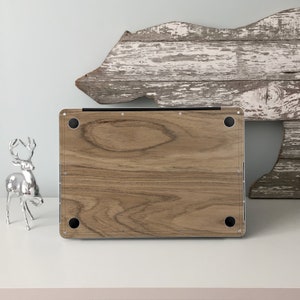 Puede incluir: Un ordenador port&aacute;til con una piel de dise&ntilde;o de grano de madera en la parte posterior. La piel es de color marr&oacute;n claro con patrones de grano de madera marr&oacute;n oscuro. El port&aacute;til est&aacute; sobre una superficie blanca.