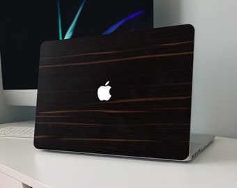 Puede incluir: Un portátil negro con un diseño de veta de madera en la tapa. El logotipo de Apple es visible en la tapa.