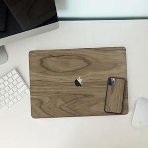 Puede incluir: Una piel para port&aacute;til y una funda para tel&eacute;fono a juego con un dise&ntilde;o de veta de madera. La piel para port&aacute;til tiene el logotipo de Apple en el centro.
