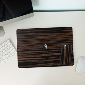 May include: A black laptop with a wood grain pattern and a matching phone case. The laptop has an Apple logo on the lid.