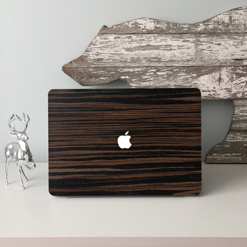 May include: A laptop computer with a dark wood grain design and a white Apple logo. The laptop is sitting on a white surface.