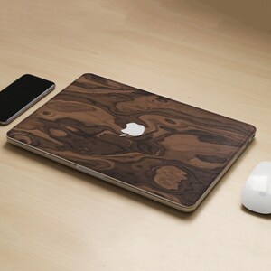 May include: A laptop computer with a wood grain design on the lid. The laptop is closed and sitting on a wooden surface. There is a white mouse and a black smartphone next to the laptop.