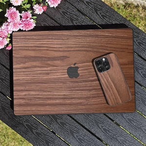 Puede incluir: Un juego de ordenador portátil y funda de teléfono de madera. El portátil tiene un acabado de veta de madera oscura con el logotipo de Apple. La funda del teléfono tiene un acabado de veta de madera a juego y un recorte para la lente de la cámara.