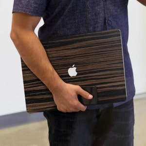 May include: A laptop computer with a wood-grain design and an Apple logo. The laptop is being held by a person.