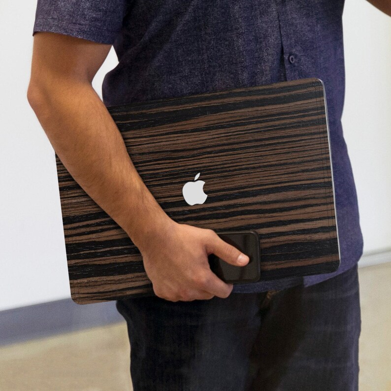 May include: A laptop computer with a wood-grain design and an Apple logo. The laptop is being held by a person.