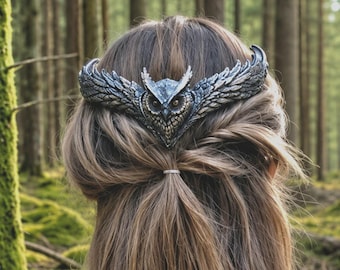 May include: A silver-toned metal hair accessory featuring an owl design. The owl has detailed feathering and large eyes, with wings extending outward. The accessory is worn on the back of the head, with long, light brown hair visible.
