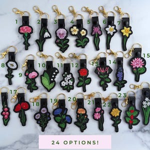 May include: Twenty-four different embroidered flower keychains with black leather and gold metal accents. Each keychain features a different flower design.