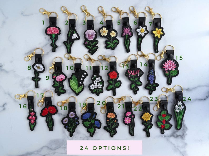 May include: Twenty-four different embroidered flower keychains with black leather and gold metal accents. Each keychain features a different flower design.