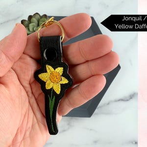 May include: A black leather keychain with a gold key ring and an embroidered yellow daffodil. Jonquil / Yellow Daffodil.