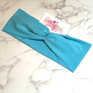 Könnte beinhalten: Ein hellblaues, geknüpftes Stirnband. Das Stirnband besteht aus einem weichen, dehnbaren Stoff. Das Stirnband liegt auf einer weißen Marmorfläche. Der Text "Sunshine Scrunchies" ist auf einer weißen Karte mit rosa Aquarell-Akzenten sichtbar.