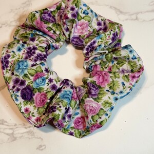 K&ouml;nnte beinhalten: Ein wei&szlig;er Haargummi mit einem Blumendruck mit rosa, lila und blauen Blumen.