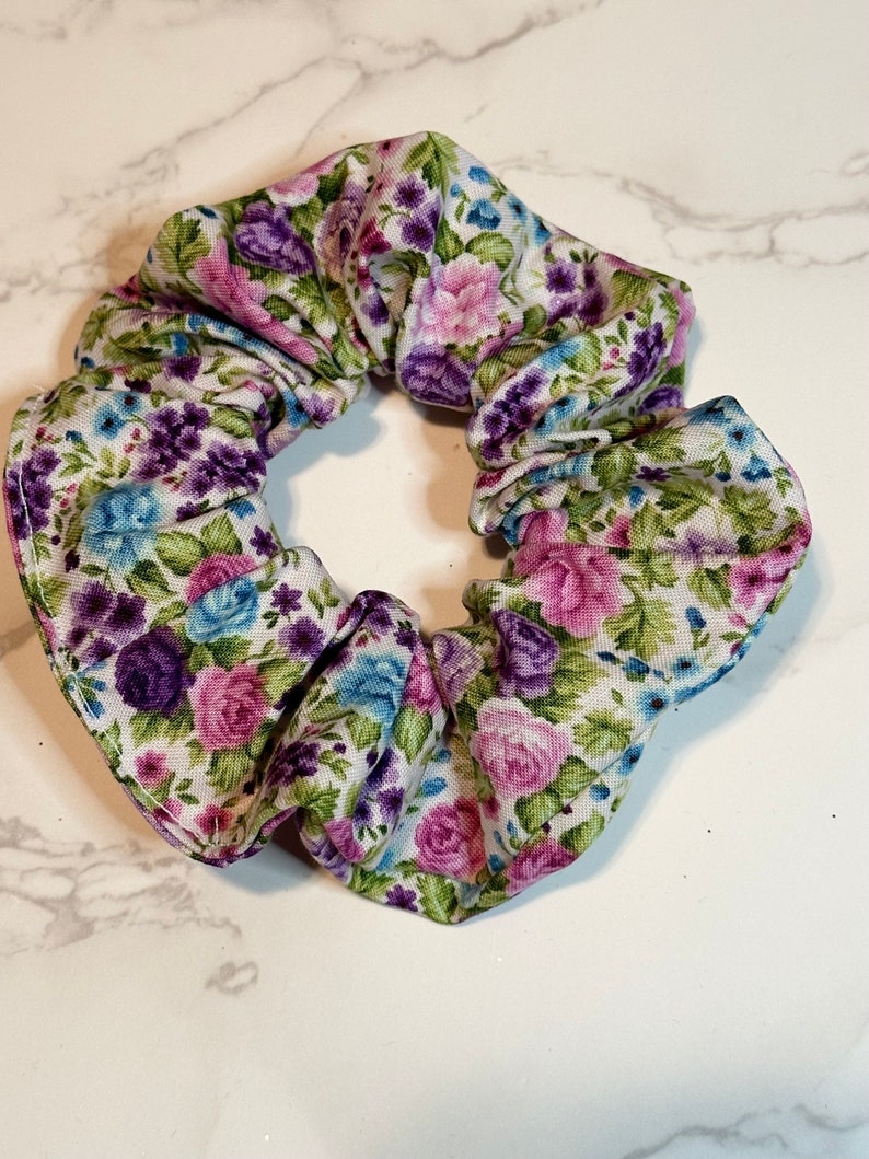 K&ouml;nnte beinhalten: Ein wei&szlig;er Haargummi mit einem Blumendruck mit rosa, lila und blauen Blumen.
