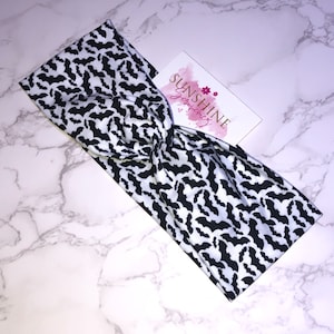 May include: Black and white headband with a bat pattern. The headband is twisted and has a white background with black bats.