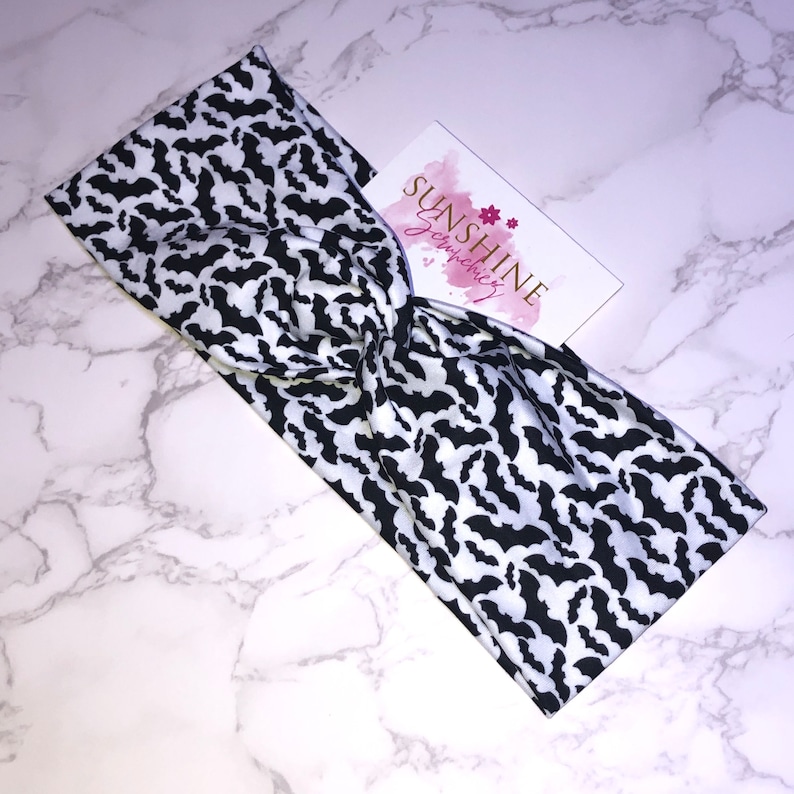 May include: Black and white headband with a bat pattern. The headband is twisted and has a white background with black bats.