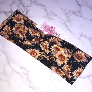 Peut inclure: Un bandeau noir avec un imprimé tournesol. Le bandeau est fait d'un tissu doux et extensible et a un design noué. Le texte "SUNSHINE Scrunchies" est visible sur une carte blanche.