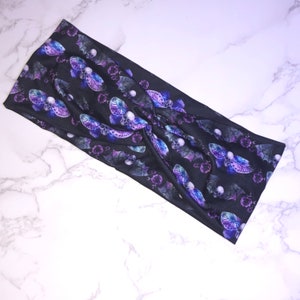 May include: A black headband with a purple and blue moth and skull pattern. The headband is made of a soft, stretchy fabric and is perfect for adding a touch of spooky style to any outfit.