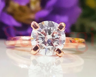 May include: A rose gold engagement ring with a round, clear center stone.