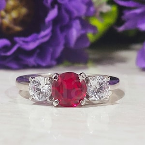 Peut inclure: Une bague en argent avec une grande pierre rouge entourée de deux petites pierres claires.