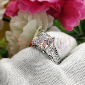 May include: A silver engagement ring featuring a large square-shaped diamond and smaller diamonds set in the band.