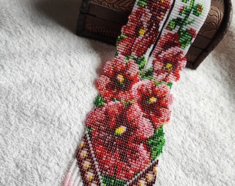 May include: A long, rectangular beaded necklace featuring a vibrant floral pattern with red, pink, and green glass beads on a white background. The piece terminates in a pointed, V-shaped end with long, dangling beaded fringe in red, pink, and green.