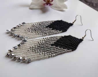May include: A pair of long, black and silver beaded earrings with a fringe of silver beads. The earrings have a geometric design and are made with small, round beads.
