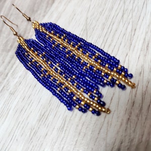 May include: A pair of long, dangling earrings made with blue and gold beads. The earrings are made with a pattern of alternating blue and gold beads.