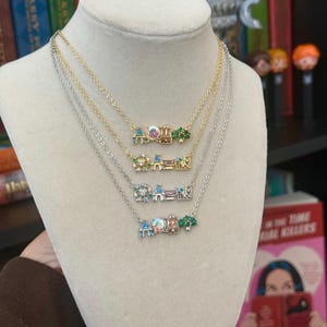 May include: Four necklaces with delicate chains and colorful pendants are displayed on a mannequin. The pendants feature miniature designs of a Ferris wheel, castle, and trees. The necklaces are gold and silver.
