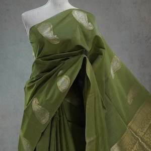 Puede incluir: Sari verde oliva con motivos de cachemira dorados y un borde dorado decorativo. La tela se drapea elegantemente, mostrando el intrincado dise&ntilde;o. Esta prenda tradicional es adecuada para ocasiones especiales.