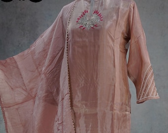 May include: A dusty rose-colored, flowing ensemble featuring a long-sleeved top with intricate embroidery around the neckline and cuffs. The outfit includes matching wide-leg pants and a draped scarf. The fabric has a subtle sheen.