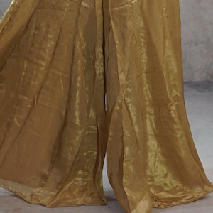 May include: Gold-colored palazzo pants made of a flowing, sheer fabric. The pants have a wide leg design and an elastic waistband. The fabric has a subtle sheen, creating a shimmering effect. The pants are suitable for dance or special occasions.