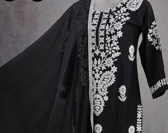 May include: Black embroidered cotton suit with a matching dupatta. The suit features white floral embroidery on the neckline, sleeves, and pants. The dupatta has a white lace trim. Sizes available: M to XXL.