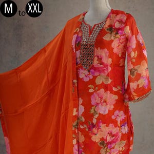 May include: A vibrant orange floral print salwar kameez ensemble. The outfit includes a long-sleeved top, matching pants, and a flowing scarf. The top features a decorative neckline. The fabric is adorned with large pink and purple flowers.