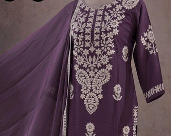May include: A plum-colored embroidered salwar kameez set. The ensemble features intricate white floral embroidery on the tunic, pants, and dupatta. The tunic has a detailed floral design on the front and sleeves. The pants and dupatta also have matching embroidery.