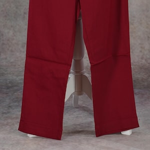 May include: A pair of wide-leg, burgundy-colored pants. The pants have a high waist with pleats and a button closure. The fabric appears to be a lightweight material, suitable for warmer weather. The pants are displayed on a white mannequin.