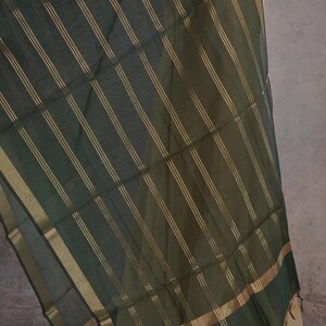 May include: Dark green sheer fabric with gold vertical stripes and gold trim. The fabric is draped over a mannequin, showcasing its flowing texture and design. The fabric has a subtle sheen.